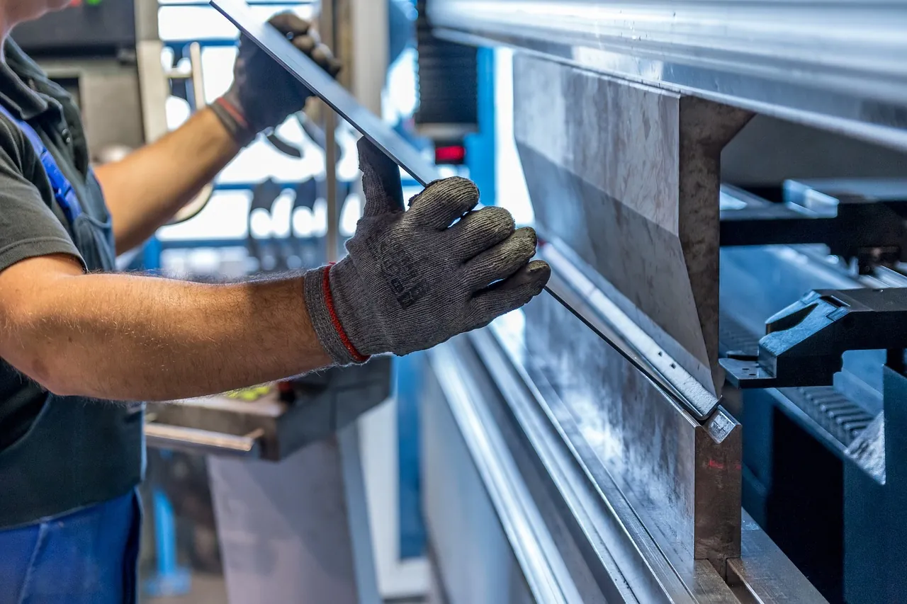 Gloved operator loading a sheet metal part into a CNC press brake